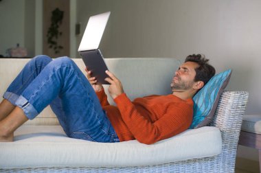 modern daire salon yazarak ve girişimci başarı ve yaşam tarzı kavramında ağ koltuk kanepe, yalan, dizüstü bilgisayar ile çalışan genç mutlu ve çekici adam rahat