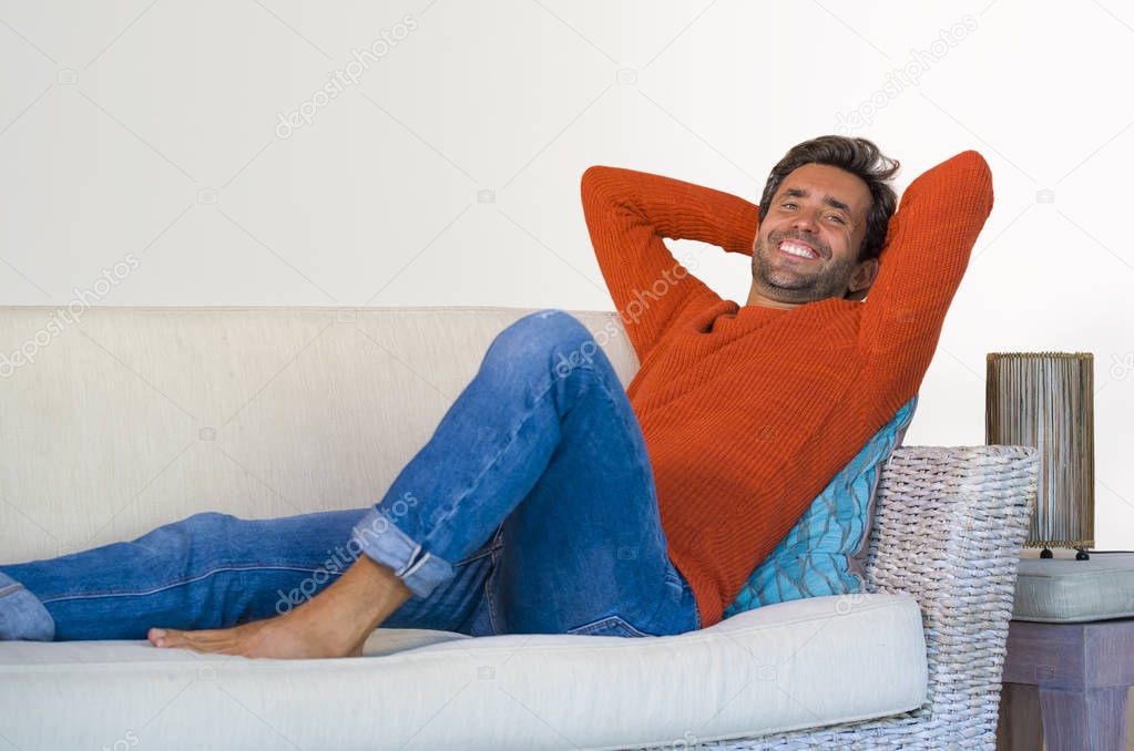 lifestyle home portrait of young attractive and happy 30s man smiling relaxed and comfortable lying at living room sofa couch in his modern apartment cheerful and positive in success concept