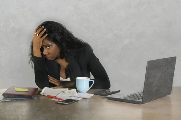 desperate and depressed black African American businesswoman crying sad at office computer desk feeling anxious and overwhelmed surrounded by mess paperwork in business stress problem