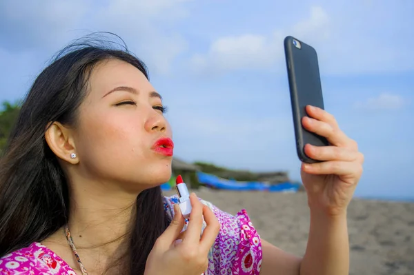 아시아 비치에서 거울으로 전화를 그녀의 입술에 립스틱을 그녀의 메이크업을 — 스톡 사진