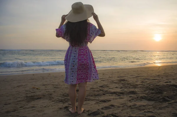 young happy and relaxed woman in Summer hat looking at the sun over the sea during an amazing beautiful sunset at tropical paradise beach in holidays travel and island tourism concept