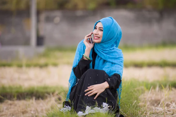 年轻美丽和愉快的穆斯林妇女穿着伊斯兰头巾头围巾和传统服装谈论手机微笑欢快的户外文化多样性与传播理念 — 图库照片