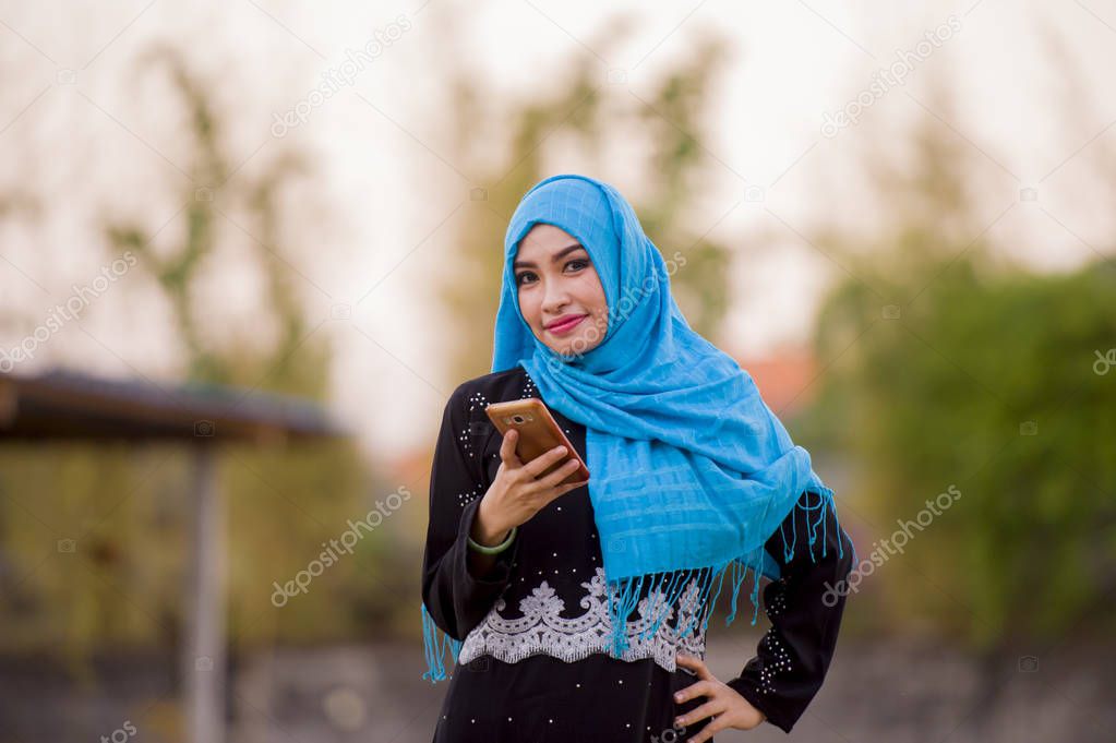 young beautiful and happy muslim woman wearing islamic hijab head scarf and traditional clothing using internet app on mobile phone smiling cheerful outdoors in culture diversity concept