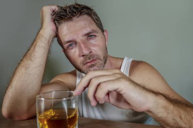 young wasted and depressed alcohol addict man in dirty singlet drinking glass of whiskey feeling desperate suffering alcoholism problem and booze addiction in alcoholic concept clipart