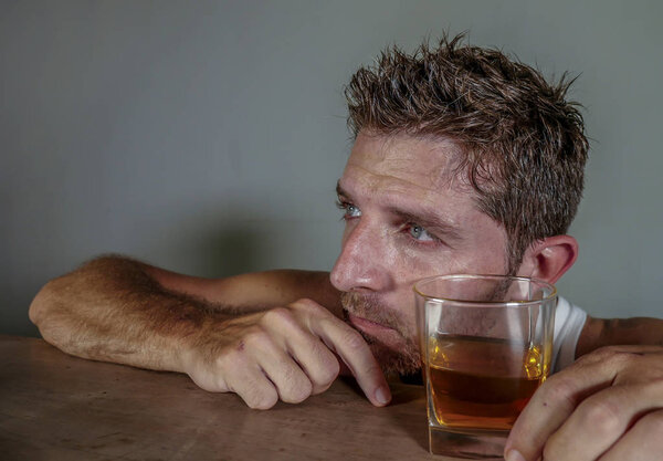 young wasted and depressed alcohol addict man in dirty singlet drinking glass of whiskey feeling desperate suffering alcoholism problem and booze addiction on isolated background in alcoholic concept