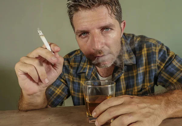 young messy and wasted addict man smoking cigarette having alcoholic drink looking at whiskey glass suffering alcoholism and tobacco addiction in unhealthy habit concept and alcohol abuse