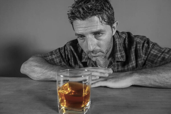 изолированный черно-белый портрет молодого грязного алкоголика, сидящего за бокалом виски и испытывающего искушение злоупотребления алкоголем в зависимости от алкоголизма
