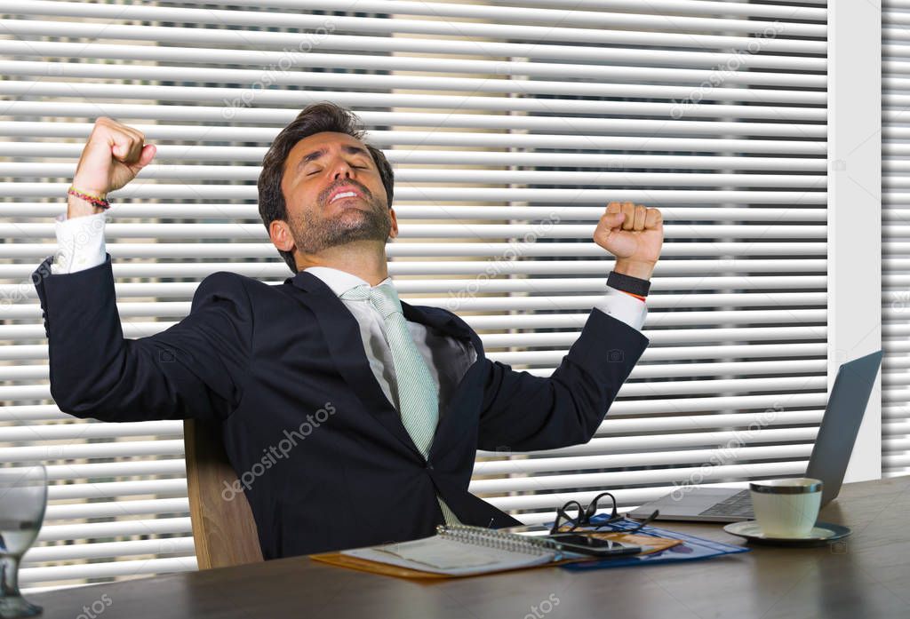 lifestyle corporate company portrait of young happy and successful business man working excited at modern office sitting by window computer desk celebrating victory in financial job success 