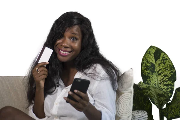 Ευτυχής και ελκυστικό μαύρο αφρικανική αμερικανική γυναίκα χρησιμοποιώντας πιστωτική κάρτα και τραπεζικό online και αγορών στο διαδίκτυο το κινητό τηλέφωνο στο σπίτι χαλαρή καναπέ-κρεβάτι — Φωτογραφία Αρχείου