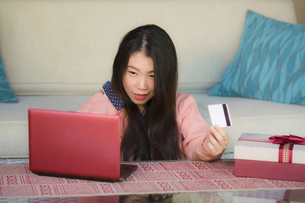 年轻美丽和快乐的亚洲女性妇女在冬季毛衣拿着信用卡和圣诞礼物盒使用笔记本电脑上网购物购买礼物从家里 — 图库照片