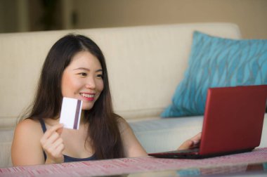internet iş ve e.commerce kavramında genç güzel yaşam tarzı portresi ve kredi kartı bankacılık ve online alışveriş dizüstü bilgisayar ile evde tutan mutlu Asyalı Çinli kadın kanepe