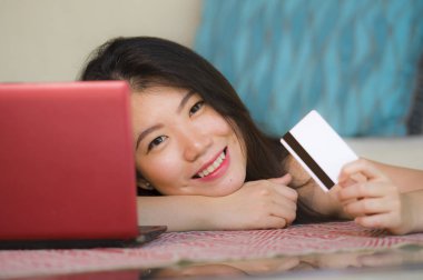 internet iş ve e.commerce kavramında kanepede genç güzel yaşam tarzı portresi ve kredi kartı bankacılık ve online alışveriş dizüstü bilgisayar ile evde tutan mutlu Asyalı Koreli kadın