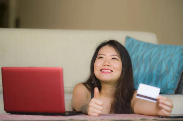 年轻美丽快乐的亚洲中国妇女持有信用卡银行和网上购物与笔记本电脑在家里的沙发在互联网业务和电子商务概念的生活方式肖像 — 图库照片