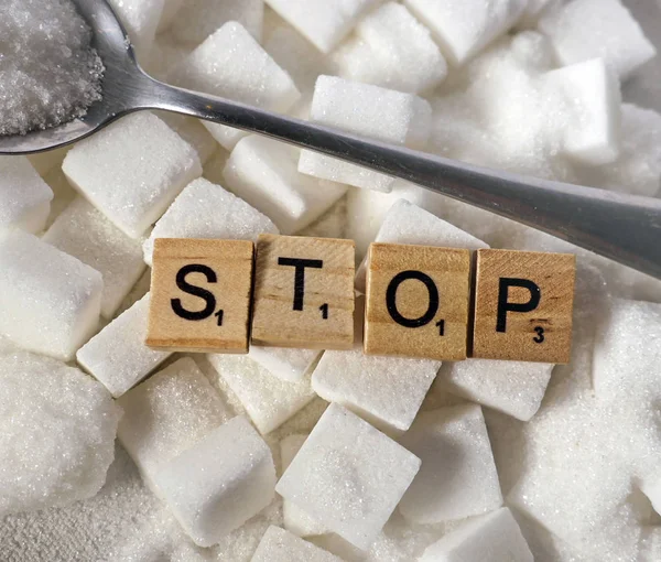 conceptual still life with pile of white sugar cubes and stop word in block letters as advise on addiction calories excess and sweet unhealthy food abuse causing health problem and overweight