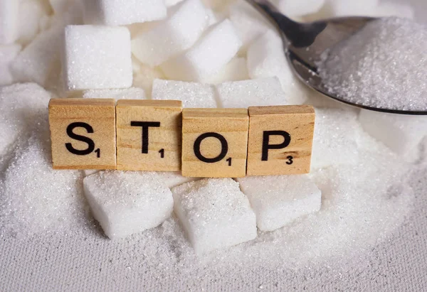 conceptual still life with pile of white sugar cubes and stop word in block letters as advise on addiction calories excess and sweet unhealthy food abuse causing health problem and overweight