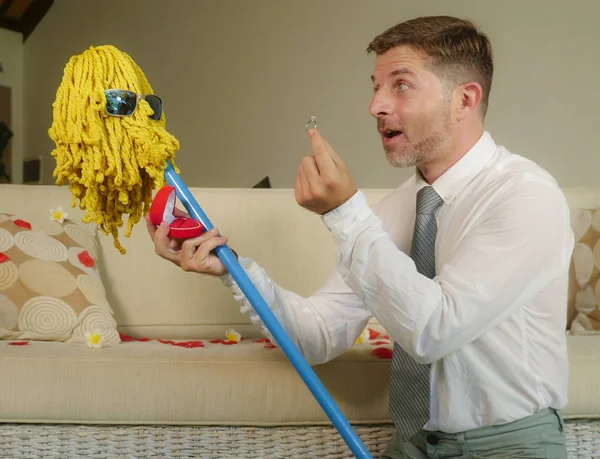 funny portrait of young weird crazy and happy man holding mop with sunglasses as if it was his fiance kneeling and proposing marriage offering engagement ring in wedding proposal parody