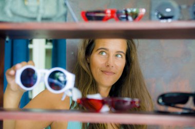 Genç güzel ve eğlenceli bir alış satış trying dışarı giysi ve güneş gözlüğü vintage ve neşeli sahip gülümseyen güzel güzellik moda mağaza alışveriş mutlu sarışın kadının 