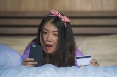 Genç güzel ve mutlu Asyalı Koreli kadın evde yatak odası ile cep telefonu e-ticaret iş neşeli yatak gülümseyen içinde kredi kartı internet bankacılığı kullanarak ve online alışveriş