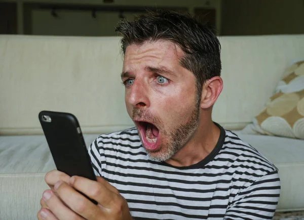 young perplexed and shocked man using mobile phone looking internet social media or checking news in surprised and crazy disbelief face expression feeling petrified and anxious