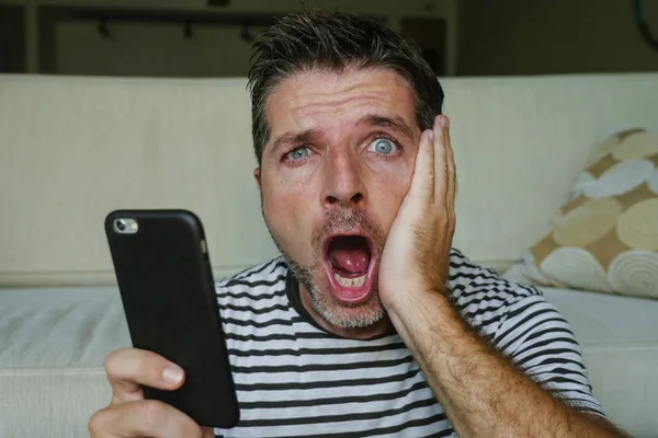 young perplexed and shocked man using mobile phone looking internet social media or checking news in surprised and crazy disbelief face expression feeling petrified and anxious