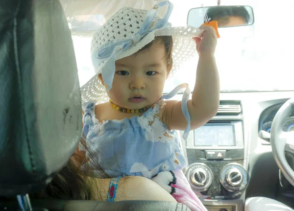 close up portrait of sweet and adorable Asian Chinese baby girl in beautiful hat hold by her mum inside a car in family lifestyle concept