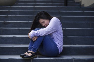 Genç üzgün ve depresyonda Asya Amerikalı öğrenci kadın ya da okulda genç sokak merdiven bunalmış ve endişeli çaresiz hissediyor açık havada oturup depresyon sorun acı 