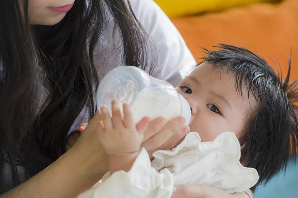 lifestyle candid portrait of young happy and sweet Asian Chinese woman feeding her beautiful baby girl with formula bottle at holidays resort as mother nursing daughter with care and love