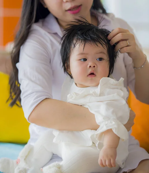 lifestyle candid portrait of young happy and cute Asian Chinese woman playing and holding sweet expressive baby girl sitting at holidays resort in mother and little daughter love concept
