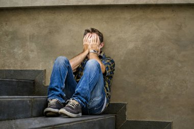 young sad and desperate man sitting outdoors at street stairs suffering anxiety and depression feeling miserable crying abandoned in unemployment and broken heart concept clipart