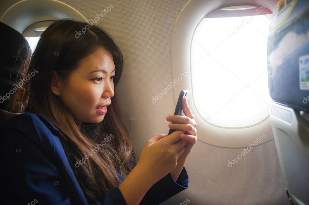 lifestyle portrait of young happy and beautiful Asian Korean woman traveling for business inside airplane cabin smiling cheerful using mobile phone in wifi and internet on flight concept