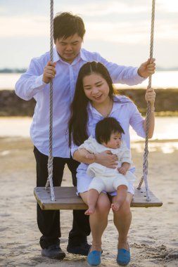 güzel ve mutlu Asya Çin ile genç çift romantik yaz tatil gezisi beach Resort eğleniyor salıncakta küçük kızını tutan anne ile zevk kız bebek 