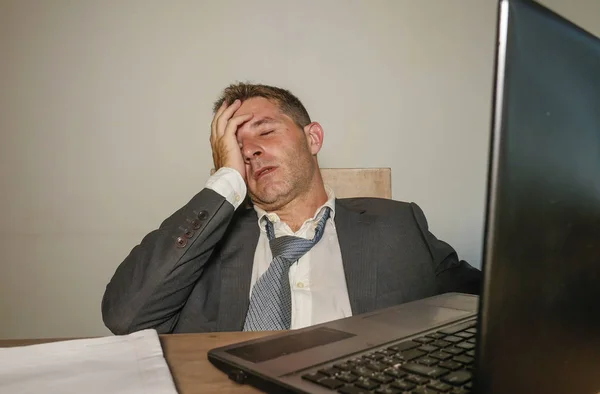 young frustrated and stressed business man in suit and tie working overwhelmed at office laptop computer desk suffering headache and migraine feeling sick in corporate job problem