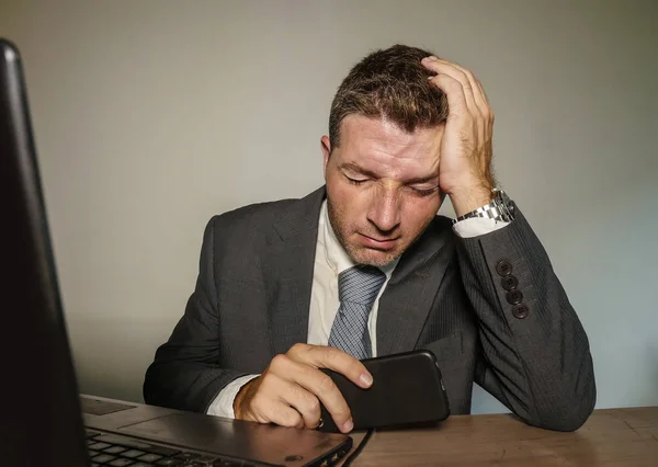 young frustrated and stressed businessman in suit and tie working overwhelmed at office laptop computer desk suffering headache and migraine feeling sick in corporate job problem