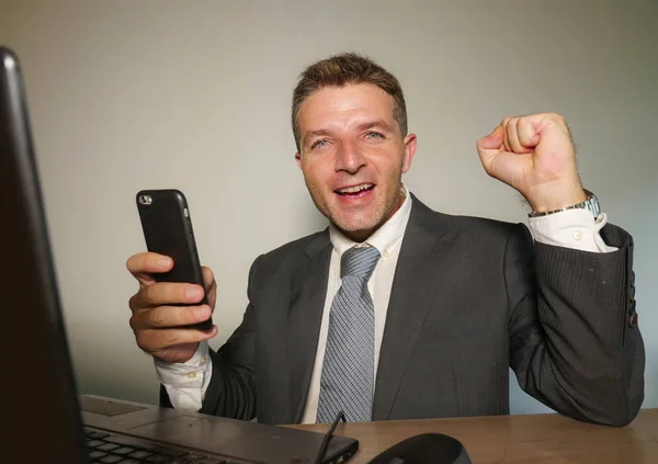 若い幸せな 魅力的なビジネス人の成功が会社の仕事の成功とエグゼクティブのライフ スタイルで興奮して身振りで示すことを祝ってオフィスのコンピューターのデスクで携帯電話を操作 — ストック写真