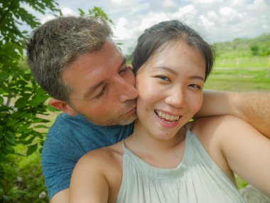 Genç güzel ve mutlu karışık etnik köken çift güzel Asyalı Çinli kadın ve beyaz adam açık havada romantik tatil zevk selfie fotoğraf çekimi aşık tropikal balayı tatil gezisi