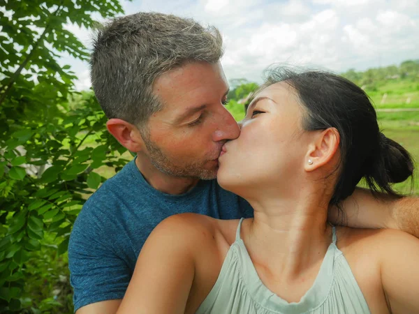 young beautiful and happy mixed ethnicity couple beautiful Asian Chinese woman and white man in love taking selfie picture outdoors enjoying romantic holidays trip in tropical honeymoon vacation