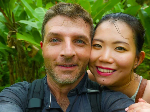 young beautiful and happy mixed ethnicity couple beautiful Asian Chinese woman and white man in love taking selfie picture outdoors enjoying romantic holidays trip in tropical honeymoon vacation