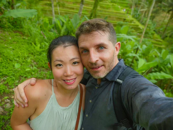 young beautiful and happy mixed ethnicity couple beautiful Asian Korean woman and white man in love taking selfie picture outdoors enjoying romantic holidays trip in tropical honeymoon vacation