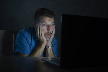 Genç adam güvensizlik ve sürpriz yüz ifadesi internette inanılmaz bir şey karanlıkta dizüstü bilgisayarla çalışma gece sürpriz ve şok izole portre