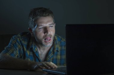 young aroused and excited sex addict man watching porn mobile online in laptop computer light night at home desk in pornography addiction and internet pornographic content concept clipart