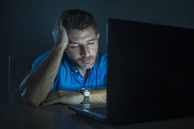 gece yarısı boşa çıkarmak ve serbest girişimci iş kavramı içinde tükenmiş karanlık duygu dizüstü bilgisayarda çalışan genç çekici ve yorgun tıraşsız adam