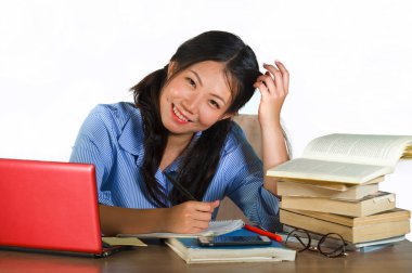 mutlu çalışma ve eğitim başarı beyaz arka plan üzerinde izole masasında oturan texbooks ve dizüstü bilgisayar ile eğitim gülümseyen genç mutlu ve sevimli Asya Çin genç öğrenci