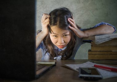 Genç stresli ve sinirli Asya dizüstü bilgisayar ve kitap yığın ile boğulmuş ve duygu yorgun masanın üzerinde çalışkan öğrenci kız yorgun ve üzerinde endişeli Korece arka plan izole