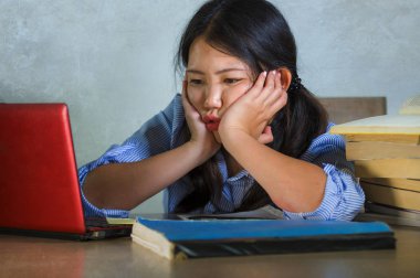 Genç stresli ve sinirli Asya dizüstü bilgisayar ve kitap yığın ile boğulmuş ve duygu yorgun masanın üzerinde çalışkan öğrenci kız yorgun ve üzerinde endişeli Korece arka plan izole