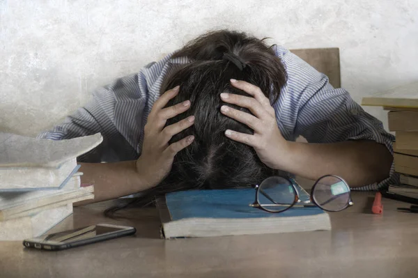 young stressed and frustrated teenager student working with textbooks and laptop computer on desk overwhelmed and exhausted leaning on table desperate worried about exam