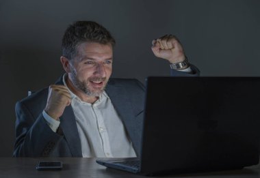 Genç mutlu ve çekici bir işadamı başarı başarılı iş ticaret veya kumar ofis dizüstü bilgisayar masası, gece geç saatlerde çalışma neşeli ve heyecanlı yüz ifadesinde kutluyor