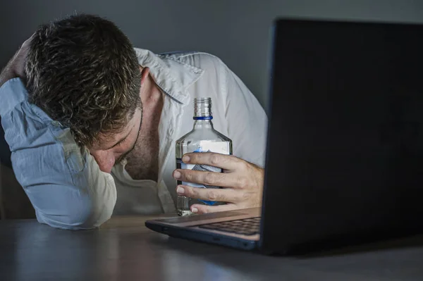 年轻的消瘦和抑郁的酗酒商人喝瓶子醉酒工作深夜在办公室笔记本电脑办公桌醉酒抑郁症和酒精中毒的问题 — 图库照片