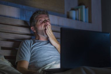 yatakta dizüstü bilgisayar esneme uykulu ve iş proje son tarih stres kavramı içinde overworked duygu ile meşgul geç gece yorgun çalışma çekici yorgun ve stresli işkolik adam