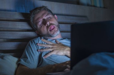 Genç adam şehvetli sapık yüz ifadesi internet porno cinsel içerik ile gece geç saatlerde seks porno film izlerken dizüstü bilgisayar kullanan cybersex oynarken yatakta yalnız uyandırdı