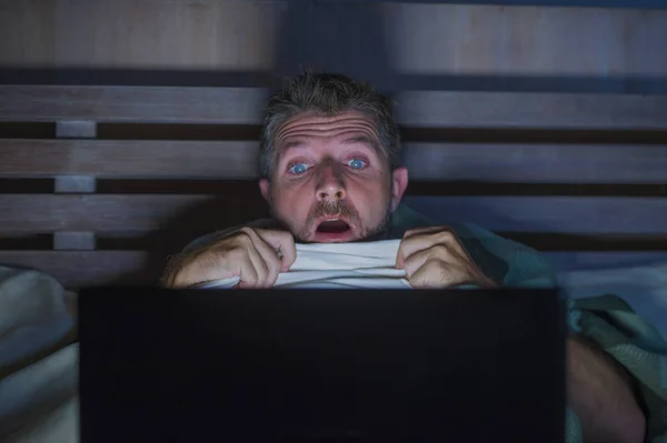 生活方式的肖像年轻的害怕和紧张的人在床上看互联网恐怖电影深夜与笔记本电脑或卧室电视在恐慌的脸表情覆盖着毯子 — 图库照片